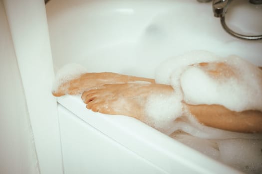 Women's feet in bath foam. View from above. Enjoy and relax in a spa hotel.