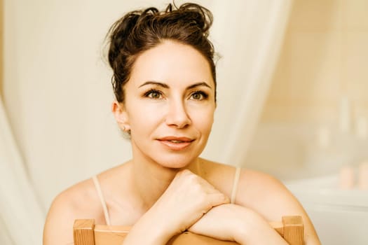 Portrait of a middle-aged woman, smiling with her arms folded in front of her face, her hair pulled up. The brunette is in a good mood. On a light background