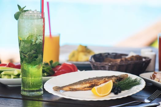Fried grayling fish on a palte with greens and lemon