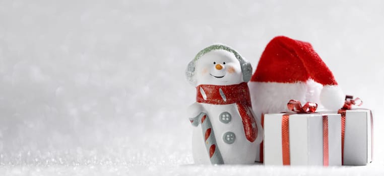 Christmas snowman with gifts and santa claus hat on bright bokeh background