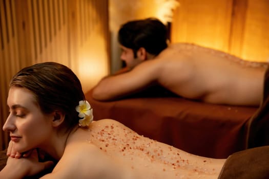 Couple customer having exfoliation treatment in luxury spa salon with warmth candle light ambient. Salt scrub beauty treatment in Health spa body scrub. Quiescent