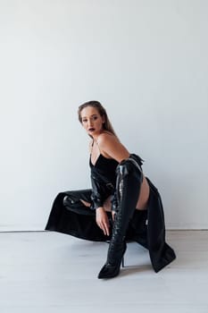 woman in a leather cloak and black clothes sits on a white background