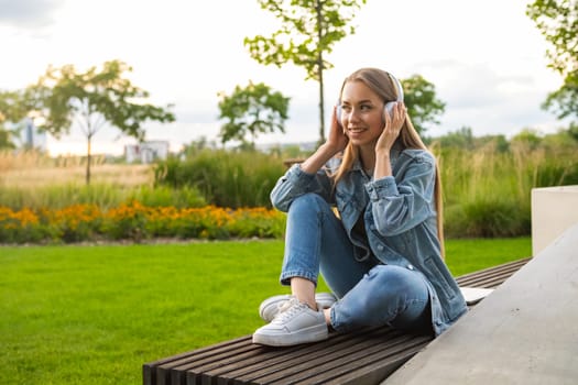 Girl with golden locks sits cross-legged on a bench, captivated by tunes playing through her headphones.