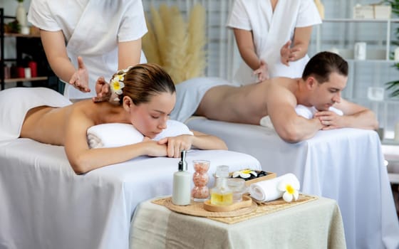 Caucasian couple customer enjoying relaxing anti-stress spa massage and pampering with beauty skin recreation leisure in day light ambient salon spa at luxury resort or hotel. Quiescent