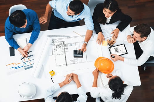 Top view banner of diverse group of civil engineer and client working together on architectural project, reviewing construction plan and building blueprint at meeting table. Prudent