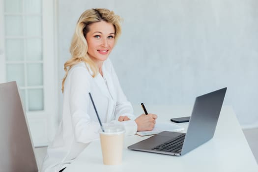 a woman in the office with a laptop computer records in a notebook remote work conversation on skype internet online communication