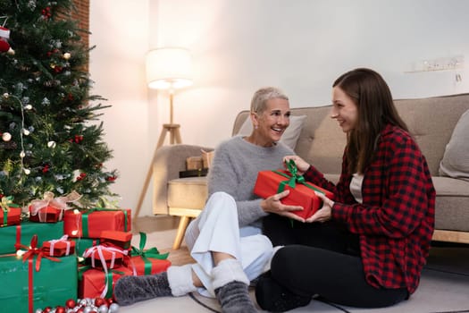 Daughter open gift from mother of Christmas while sitting on floor at home.