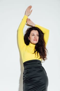 brunette woman stands against a white wall with her hands up