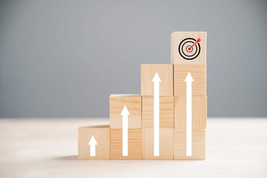 Cube wood blocks featuring prominent Target icon and rise up arrows. Bar graph chart steps on vertical background signify business growth process, emphasizing profit, investment, economic improvement
