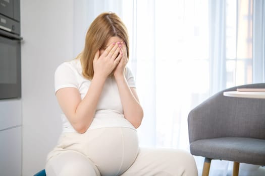 Tired pregnant woman closes her face with her hands.