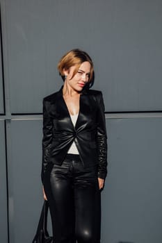 a fashionable woman in leather black clothes near the black wall of the building