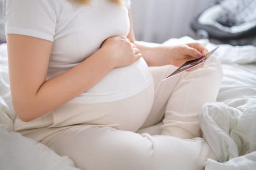 Pregnant woman holding UZ photo of baby near belly. Expecting of baby