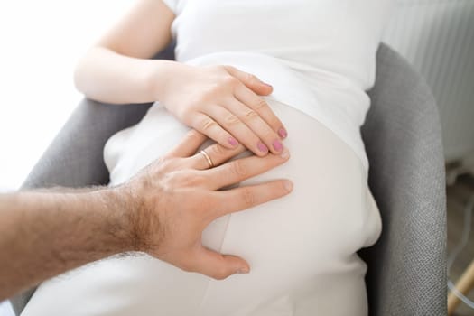 Mans and womans hands on the pregnant stomach. Expecting baby.