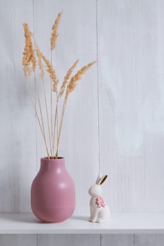 The shelf decor consists of a pink vase with dried flowers and a white porcelain rabbit with a pink bow with copy space