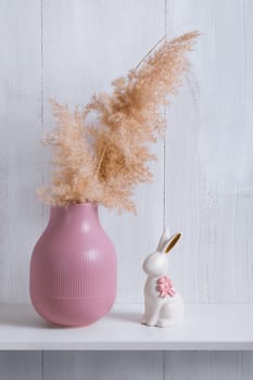 The decor elements of a bright room in an eco-style are a shelf with a pink vase, a reed and a porcelain rabbit