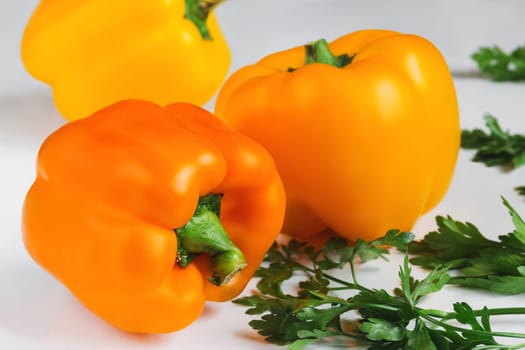 Three ripe orange sweet peppers and fresh green juicy parsley on a white table