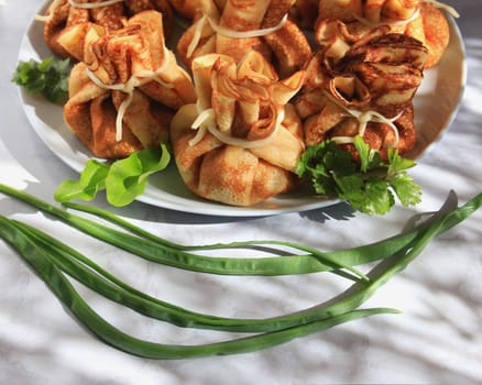 Pancakes with filling in the form of bags tied with cheese, close-up. A traditional dish for the Maslenitsa