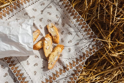 Almond cookies crackers with pieces of nuts fell out of a paper bag on a napkin lying on the straw, top view