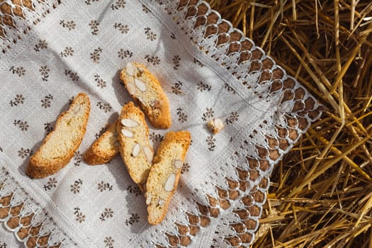 Almond cookies crackers with pieces of nuts lie on a napkin against a background of straw, top view