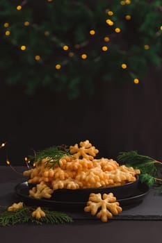 Cookies Brushwood in the form of snowflakes lie in a slide on a black plate in a Christmas decoration, with copy space