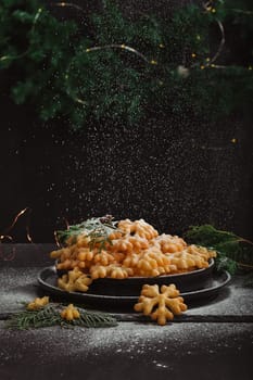 Cookies Brushwood in the form of snowflakes, sprinkled with powdered sugar, lies in a pile on a black plate, with copy space. Delicious, tender and crunchy treat for the holiday