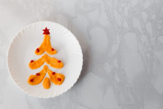 Squash caviar on a white plate in the shape of a Christmas tree decorated with balloons and a ketchup star. Alternative Christmas tree made of food with copy space