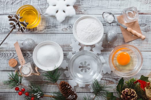 Recipe for making cookies brushwood on a light wooden background with Christmas decorations. The prepared ingredients include butter, water, salt, sugar, vodka, water, egg, flour. Top view