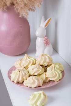 Sweet treat for the holiday - meringue on a plate on the background of a vase and a porcelain rabbit