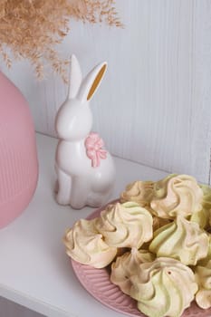 Yellow-pink meringue on a pink plate and a white porcelain rabbit with a bow