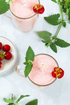 Milkshake with strawberries in a glass glass with melissa leaves in the design, top view