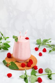 Milkshake with raspberries in a glass glass with melissa leaves in the design with copy space