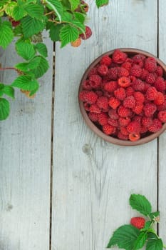 Raspberry berry fresh in a clay plate on a wooden background, top view