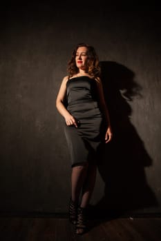 woman in a black dress stands in a dark room