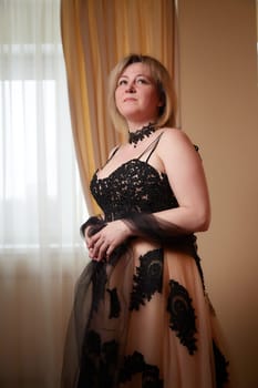 Portrait of beautiful elegant woman in in a royal dress indoors in nice room in evening time. Middle-aged adult lady in a romantic setting