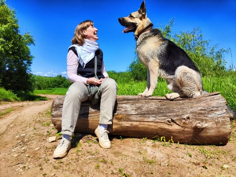 Dog German Shepherd and woman on a log in nature in summer or spring day. Russian eastern European dog and the mistress, trainer veo outside and outdoors