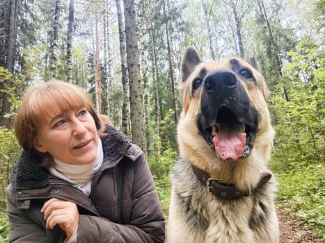 Adult girl with shepherd dog taking selfies in forest. Middle aged woman and big shepherd dog on nature. Friendship, love, communication, fun, hugs