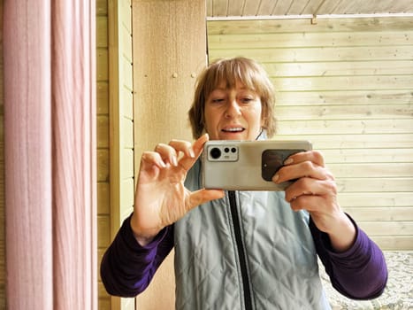 Middle-aged woman using smartphone for selfie and blogging. Female blogger poses in a photo. The girl admires herself in the mirror