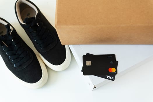 Black sneakers, cardboard box and Visa credit card on a white table. Purchase with a card via the Internet