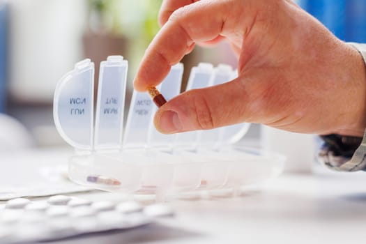 Male hand putting pills into open pill organizer or plastic pillbox. Sorting of tablets for daily use according to a doctor's prescription