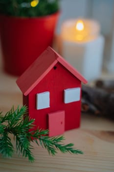Wooden red house to decorate the house for the Christmas holidays. Wooden toy for the Christmas tree. A candle in a jar is burning in the background. Juniper branches. A product handmade.