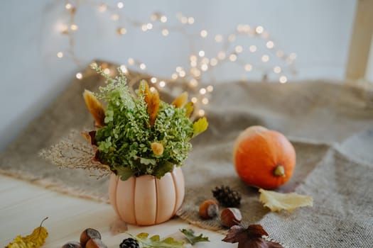 Autumn composition of books, pumpkins, nuts, autumn leaves, a bouquet of dried flowers, cones. Pumpkin and nuts. Garland with warm light. Bokeh. Thanksgiving Day. Festive composition.