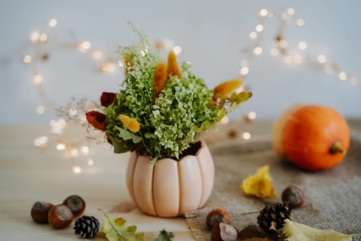 Autumn composition of pumpkins, nuts, autumn leaves, a bouquet of dried flowers, cones. Pumpkin and nuts. Garland with warm light. Yellow Bokeh. Thanksgiving Day.