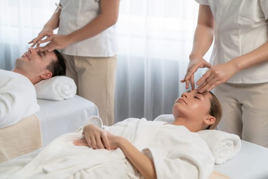 Caucasian couple enjoying relaxing anti-stress head massage and pampering facial beauty skin recreation leisure in dayspa modern light ambient at luxury resort or hotel spa salon. Quiescent