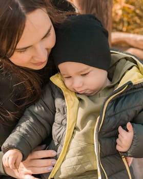 Cute little boy stands with mother outdoors. Happy child walking in autumn park. Toddler baby boy wears trendy jacket and hat. Autumn fashion. Stylish child outside