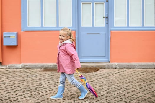 A girl in rubber boots and an umbrella is walking on the pavement