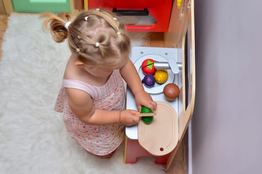 Girl cuts wooden vegetables on toy kitchen wooden cooking toy.