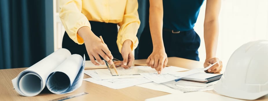 Professional architect team used divider measure during draft blueprint on table with architectural document, safety helmet and blueprint scatter around. Closeup. Focus on hand. Delineation.