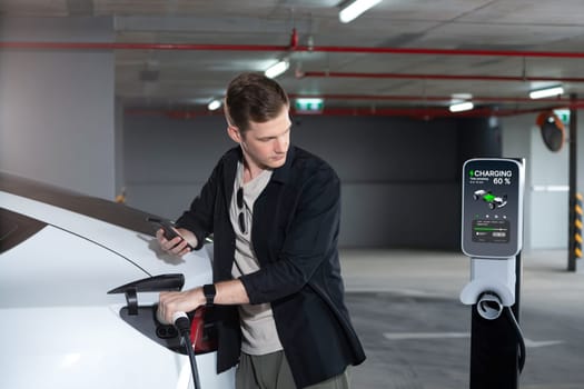 Young man travel with EV electric car to shopping center parking lot charging in downtown city showing urban sustainability lifestyle by green clean rechargeable energy of electric vehicle innards