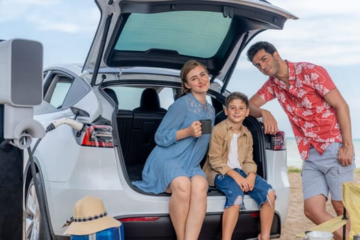 Family vacation trip traveling by the beach with electric car, happy family recharge EV car, enjoying outdoor camping coffee. Seascape travel and eco-friendly car for clean environment. Perpetual