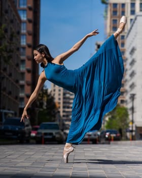 Beautiful Asian ballerina in blue dress posing in splits outdoors. Urban landscape. Vertical photo